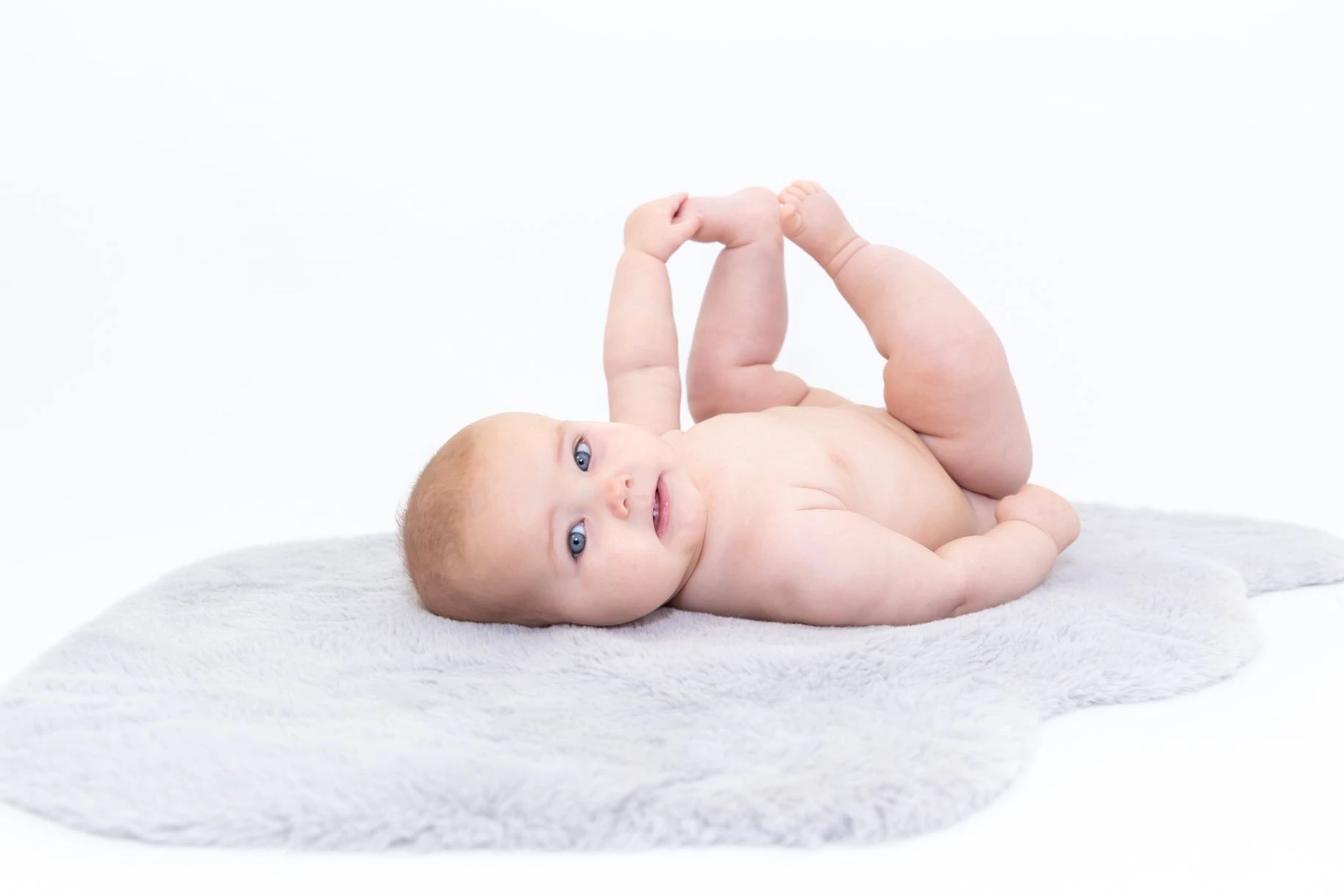 6 month old baby lying on back holding their foot