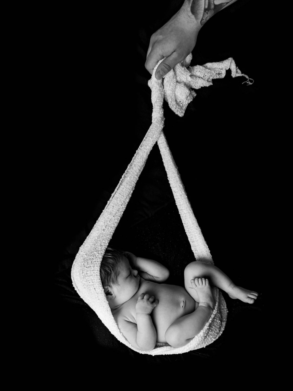 Newborn baby hanging in hammock being held by dad